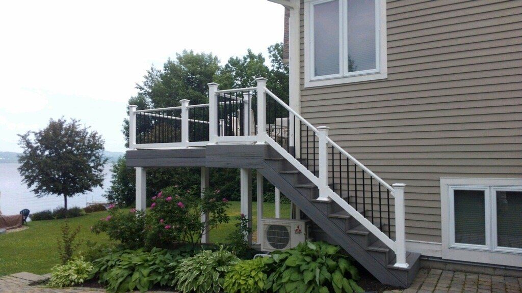 House exterior with white-railed deck and stairs beside a garden and waterfront view