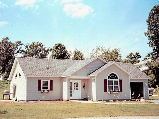 Single-story beige house with white trim, front porch, and attached garage under a blue sky