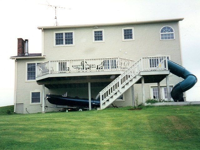 Two-story house with a large deck, exterior stairs, and a blue slide on a grassy lawn.