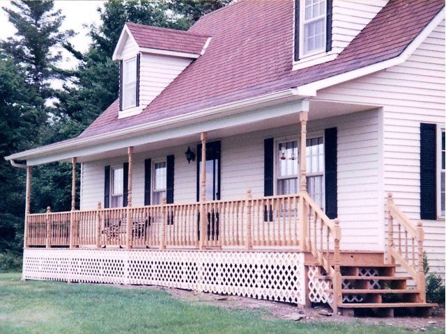 White farmhouse-style house with a wraparound porch, red roof, and stairs on the right