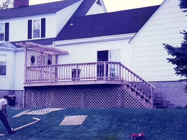 Backyard deck attached to a house with stairs, lattice skirting, and a green lawn
