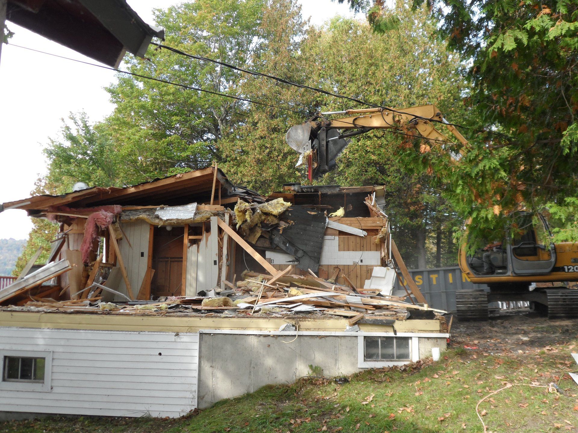 A house is being demolished by a yellow excavator