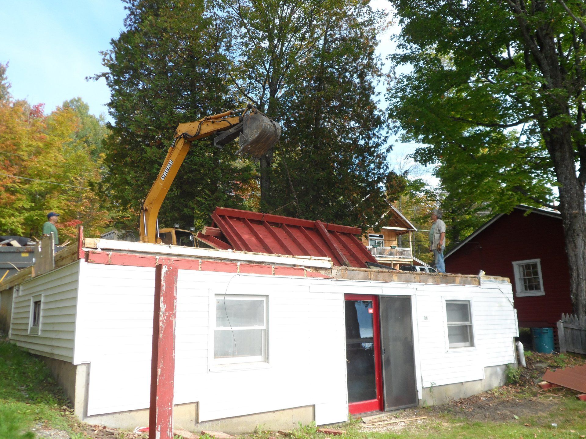 A bulldozer is demolishing a white house with a red door