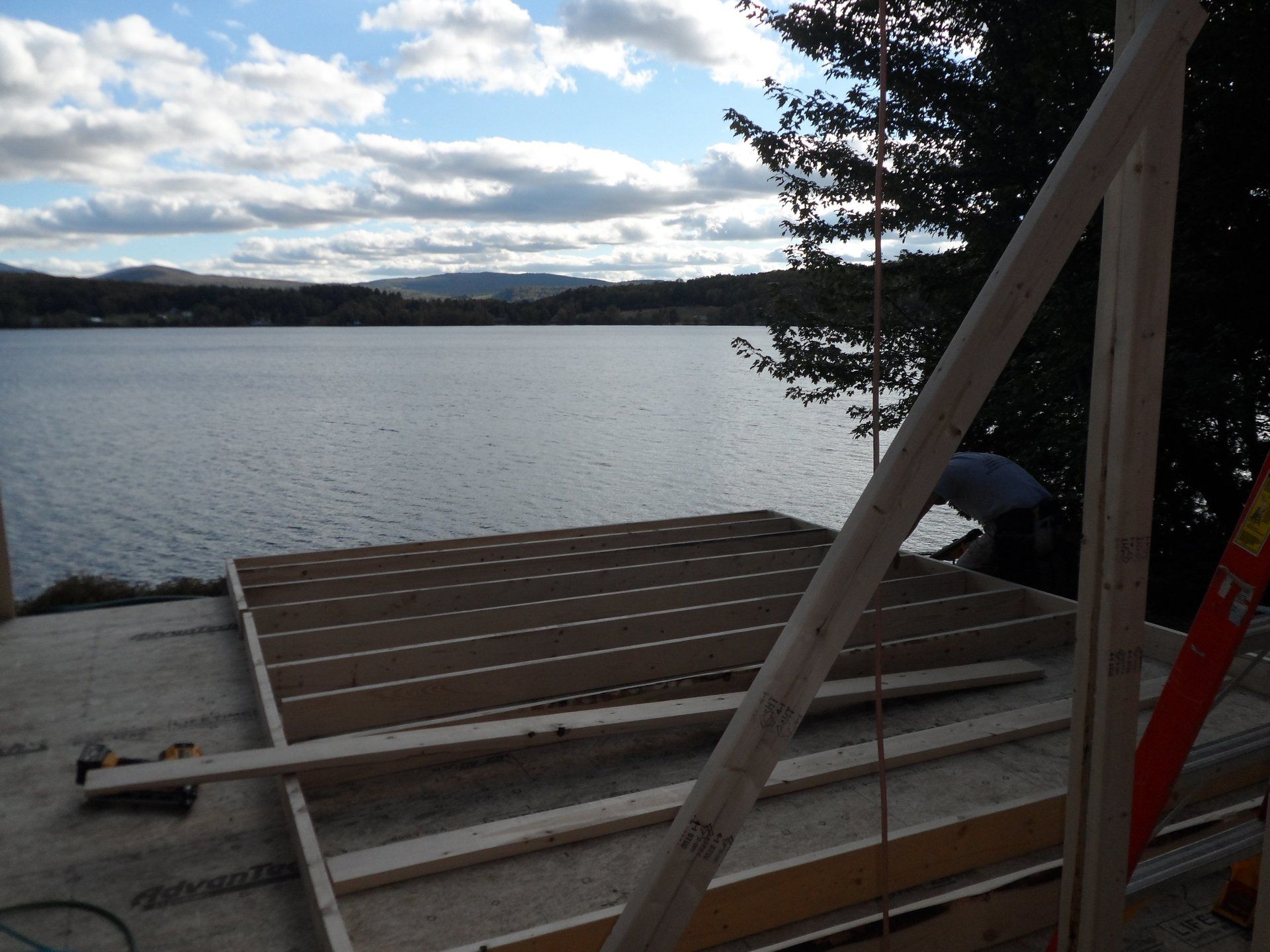 A man is working on a wooden deck overlooking a lake