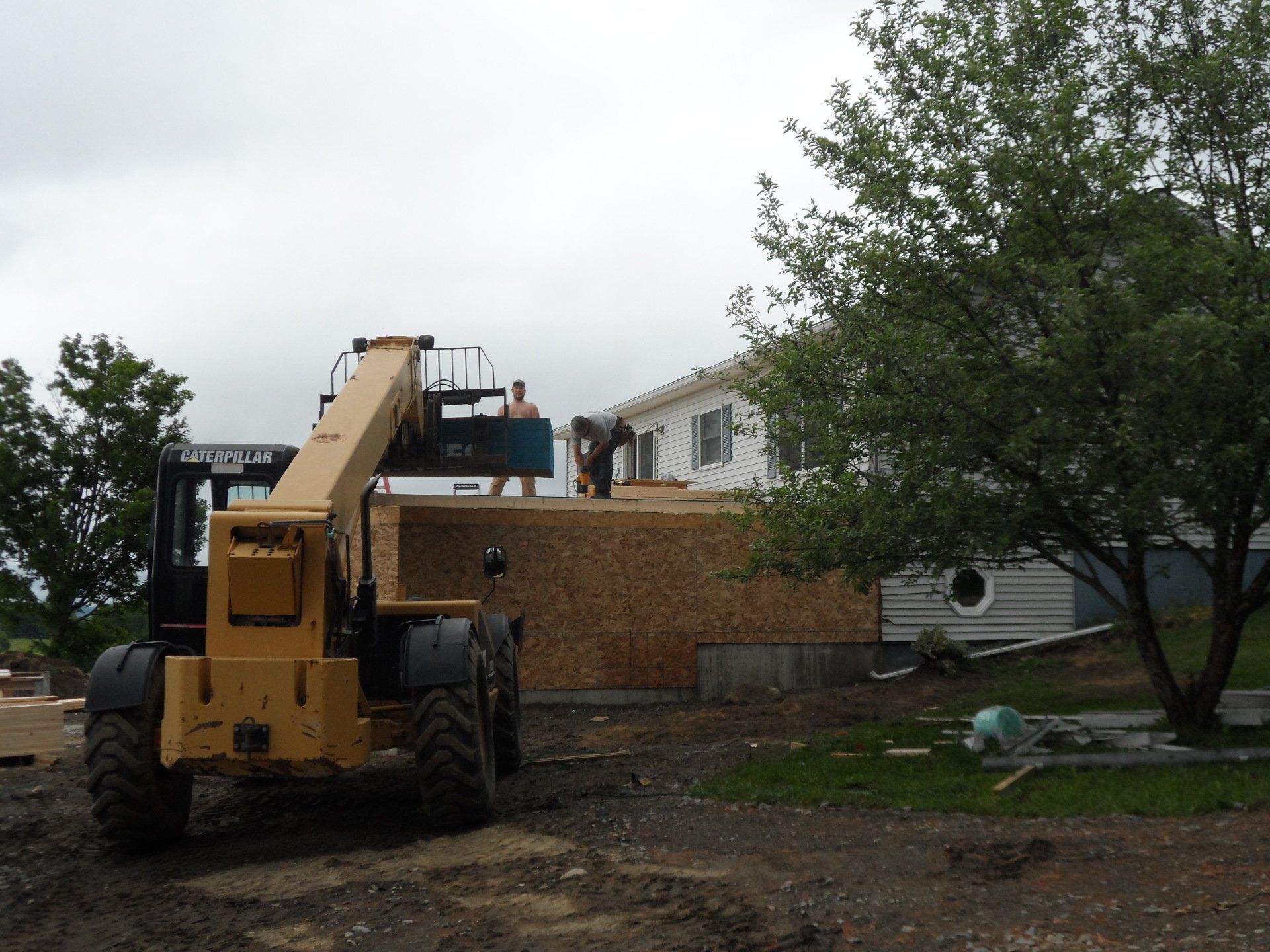 Yellow construction lift parked beside a brick house under cloudy skies