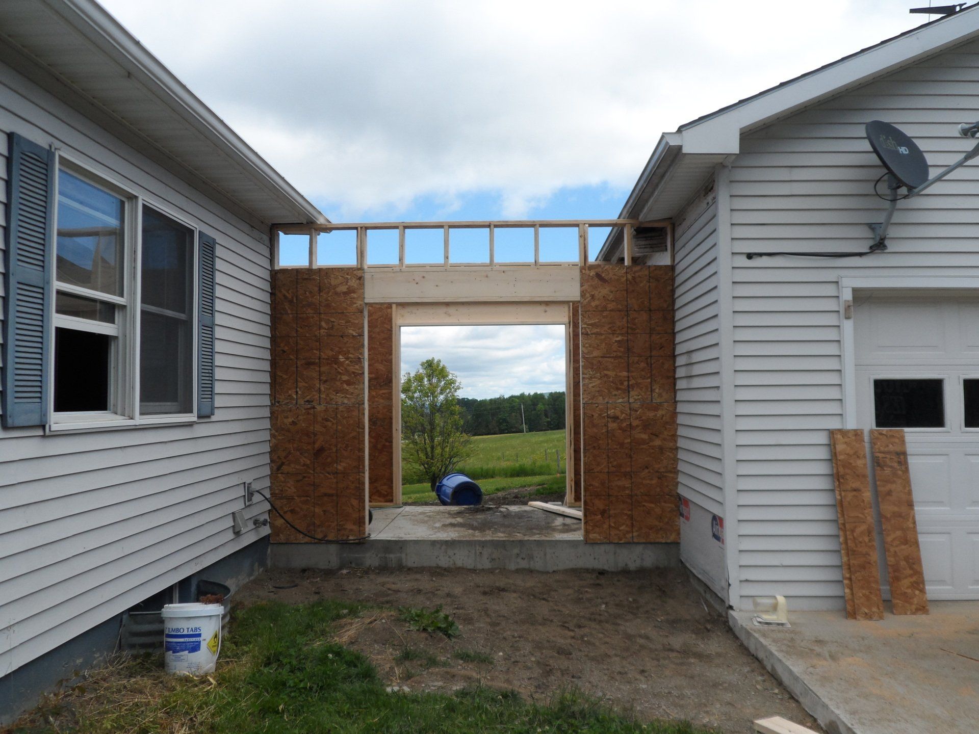 Partially built brick passageway between two white houses, with a view of green fields beyond.