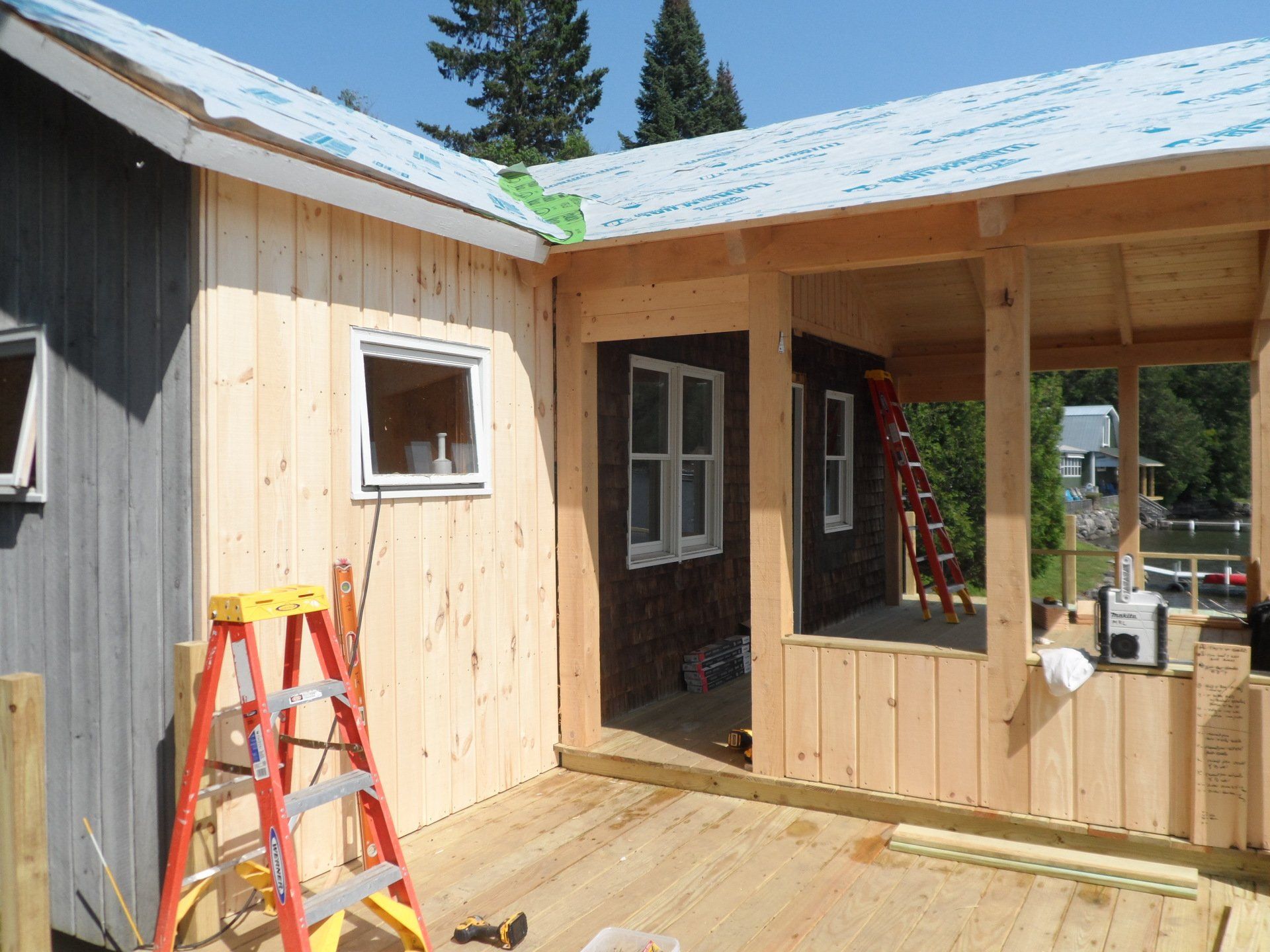 Wooden house under construction with ladders, porch framing, and a partially finished roof