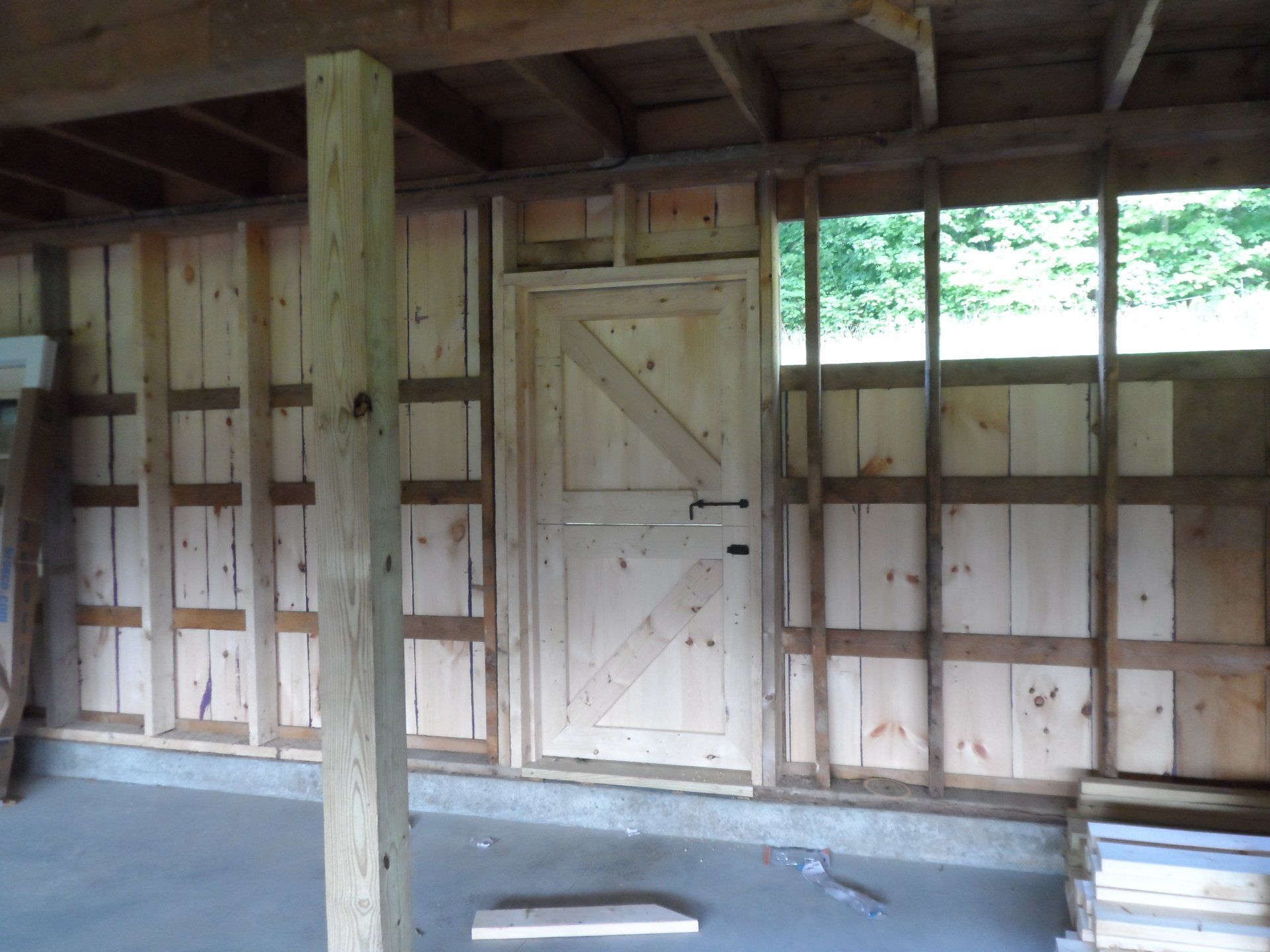 Interior view of a barn under construction: wooden walls, a door, and support beams.