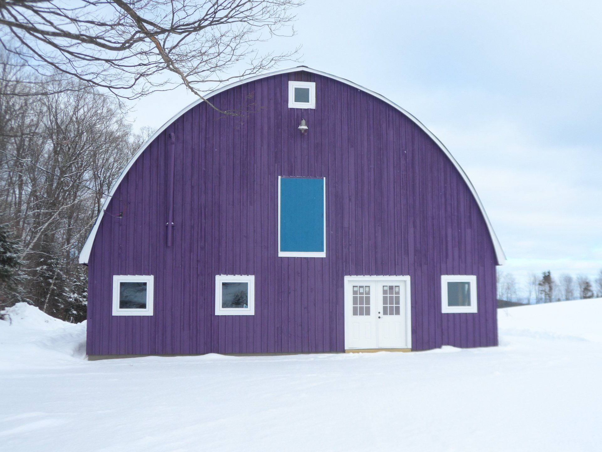 Purple barn in snow with white windows and doors.