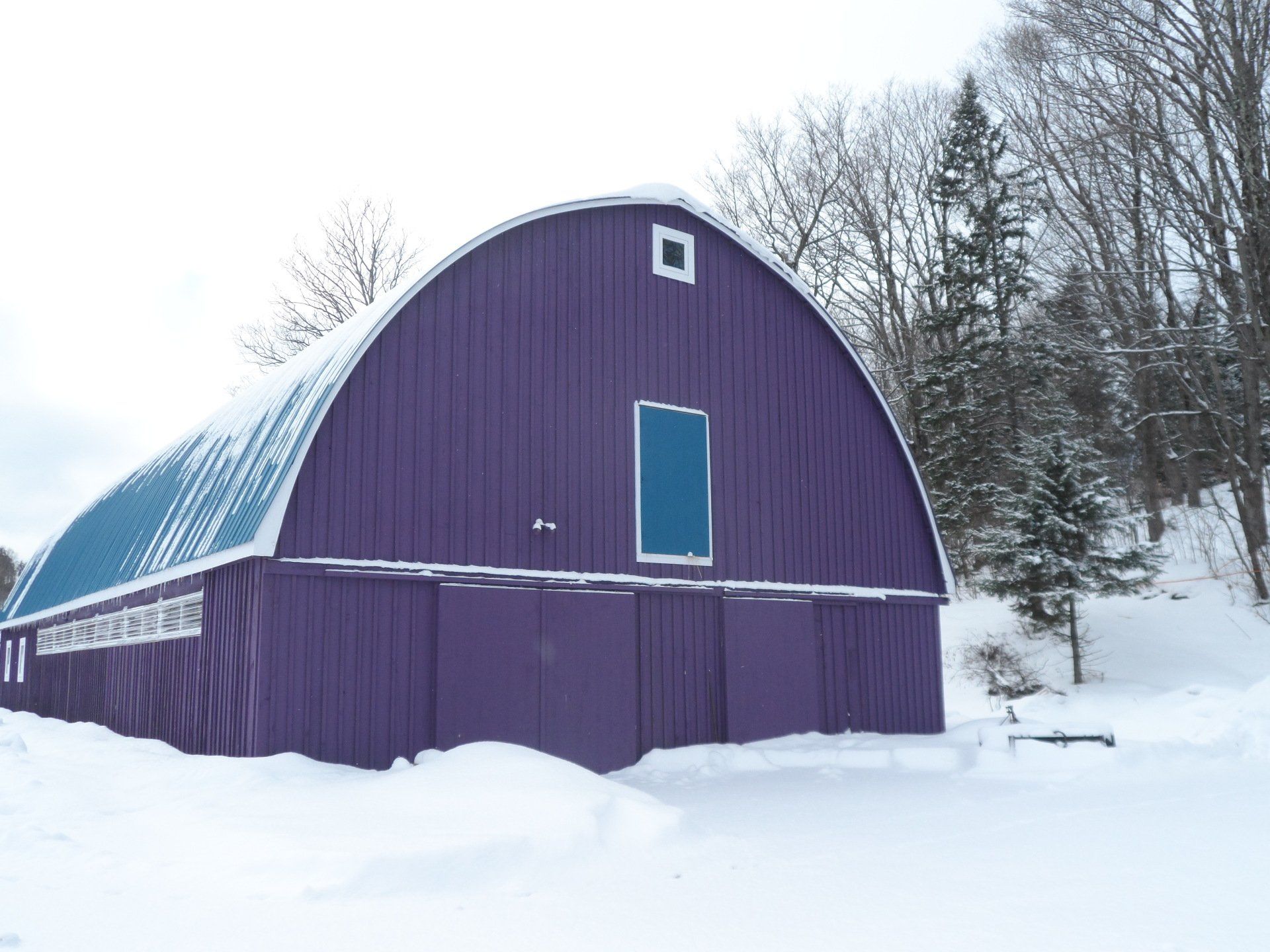 Purple arched barn in snow with blue roof.