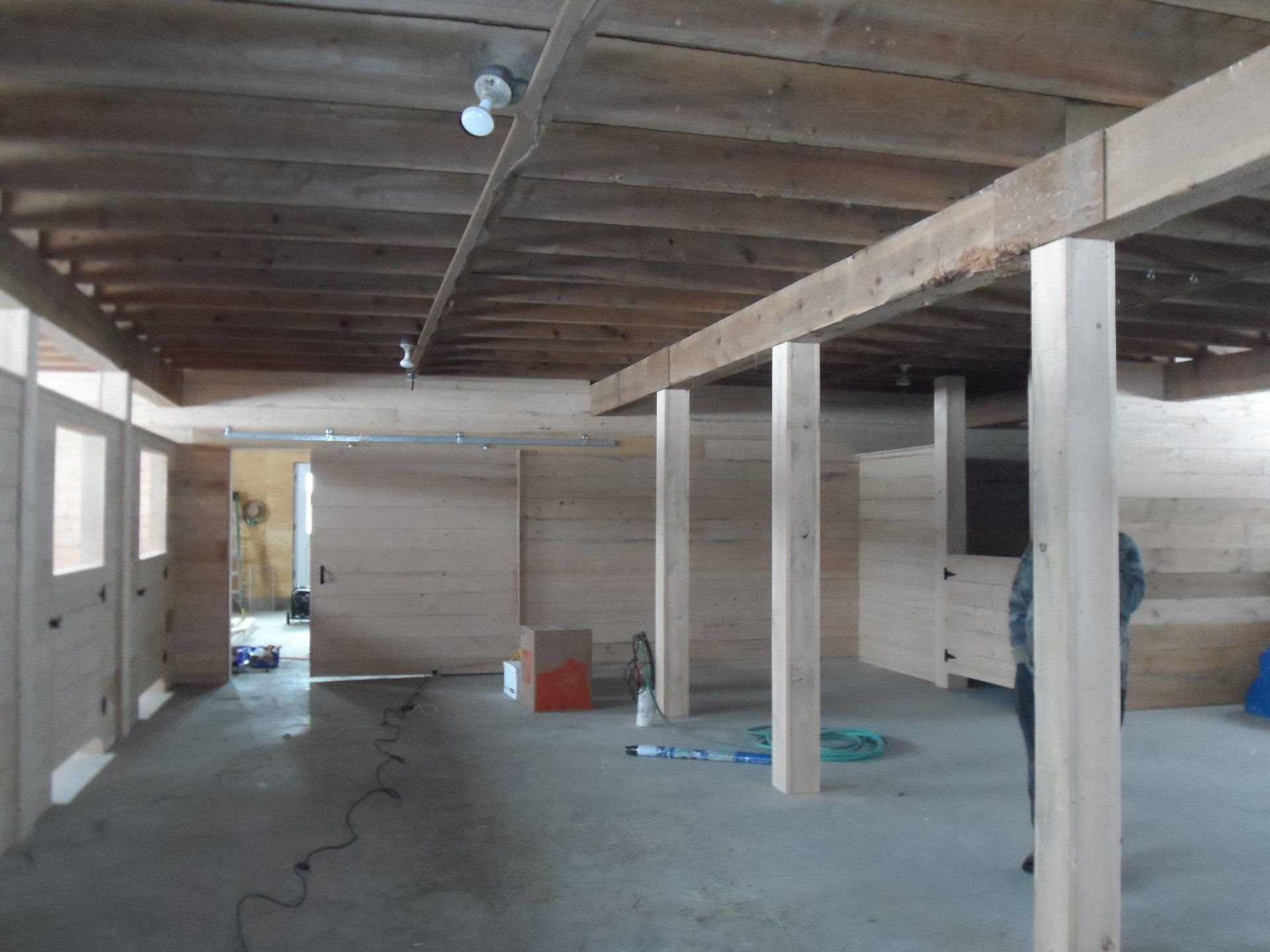 Interior of a building under construction, showing wooden beams, walls, and a concrete floor.