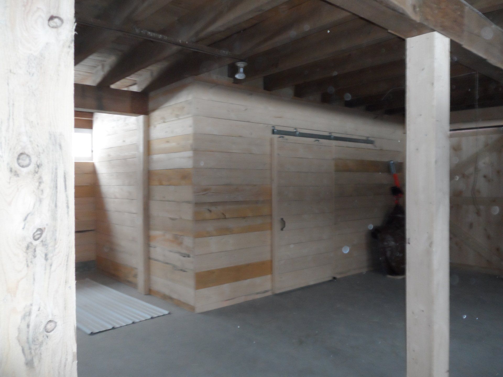 Interior view of a room with light-colored wooden walls and support beams, featuring a rectangular structure.