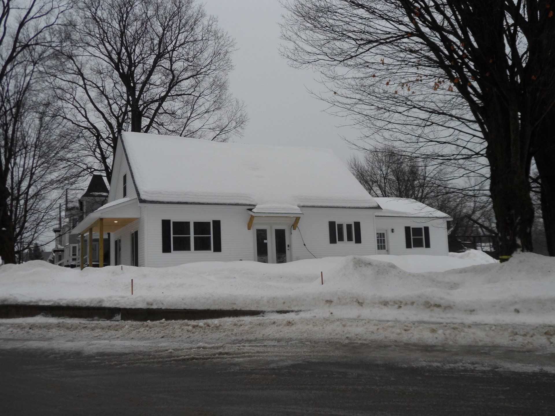 A white house with snow on the roof and trees in the background