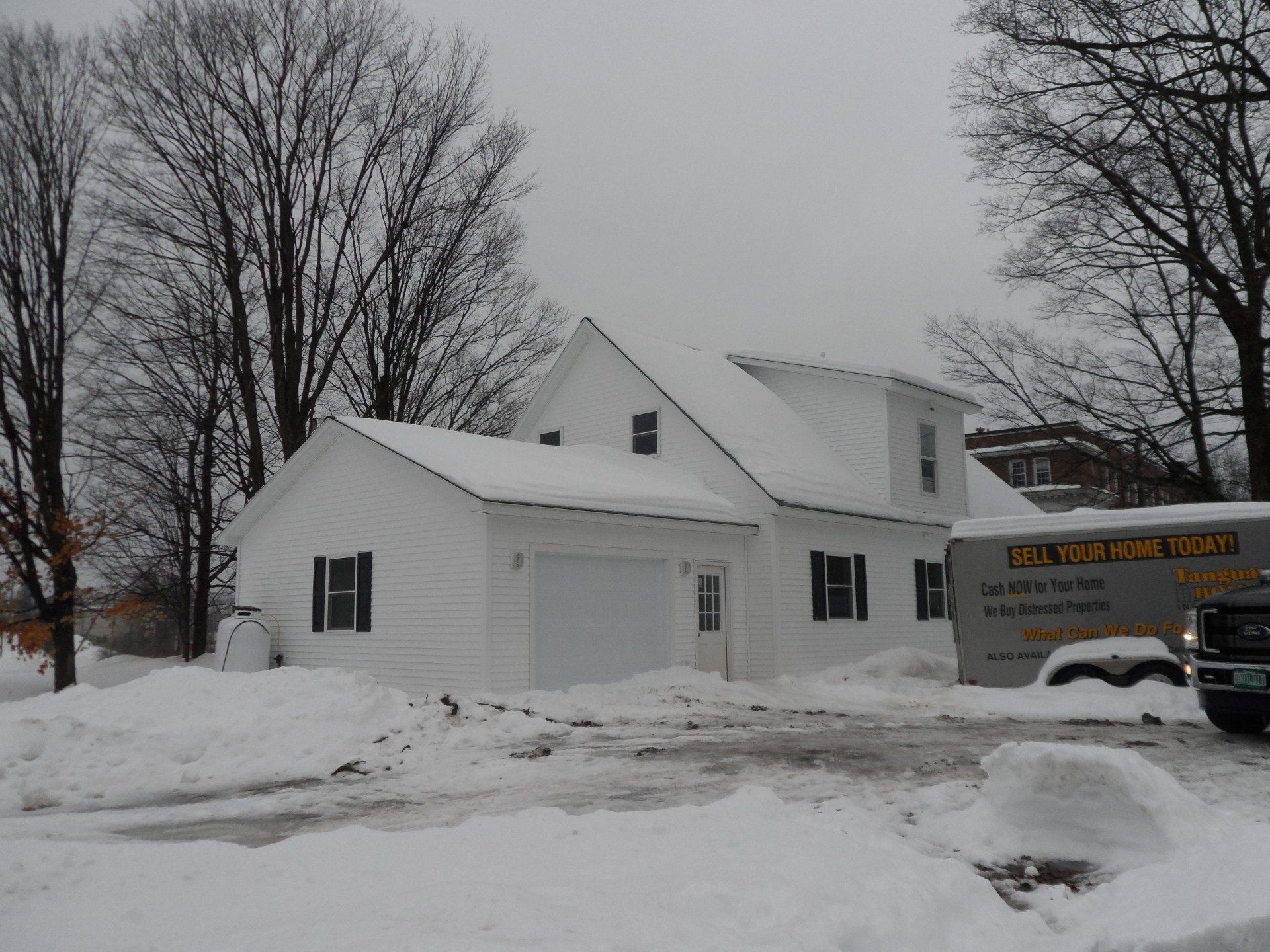 A white house is covered in snow and a truck is parked in front of it