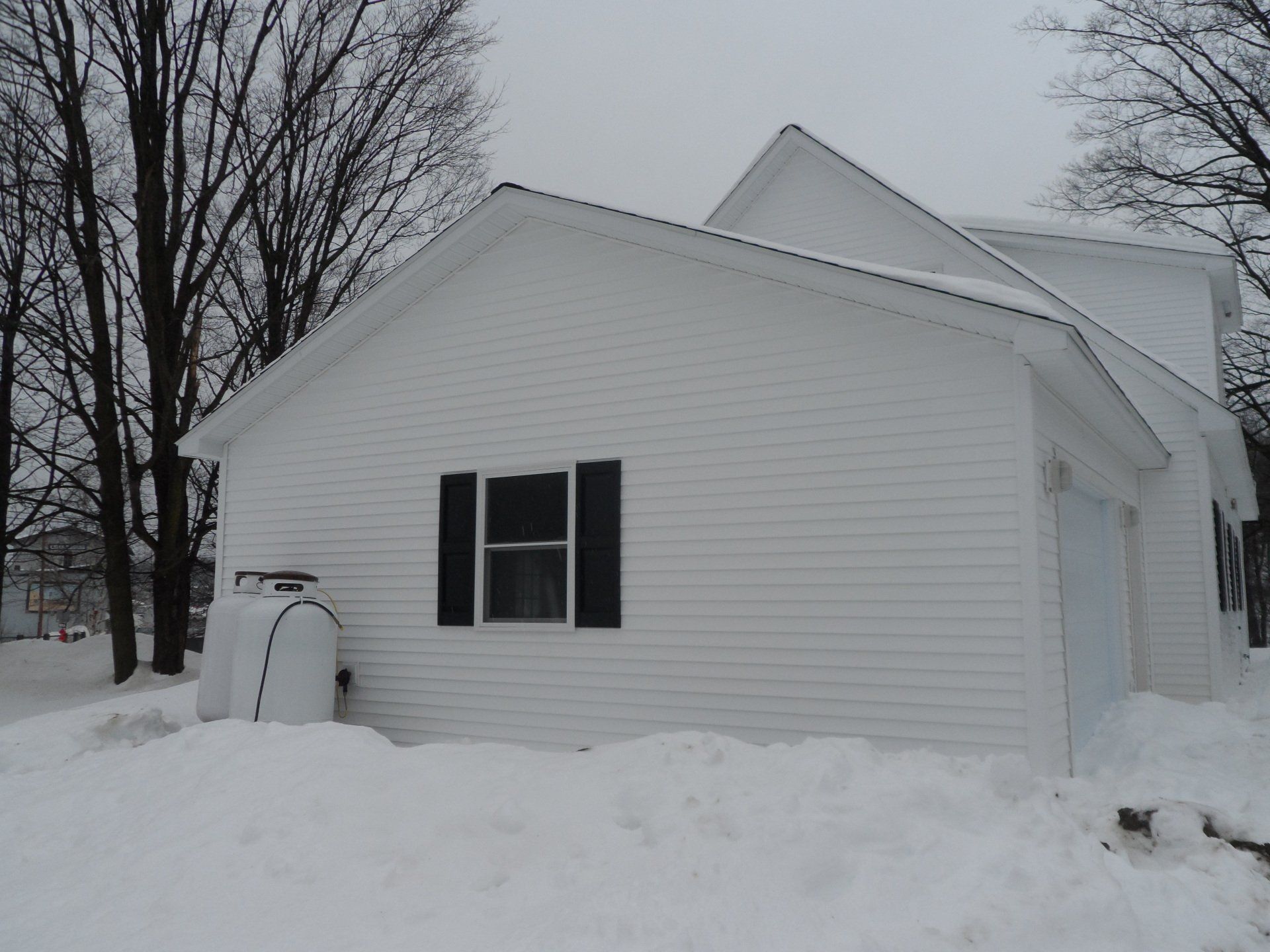 A white house with black shutters is covered in snow