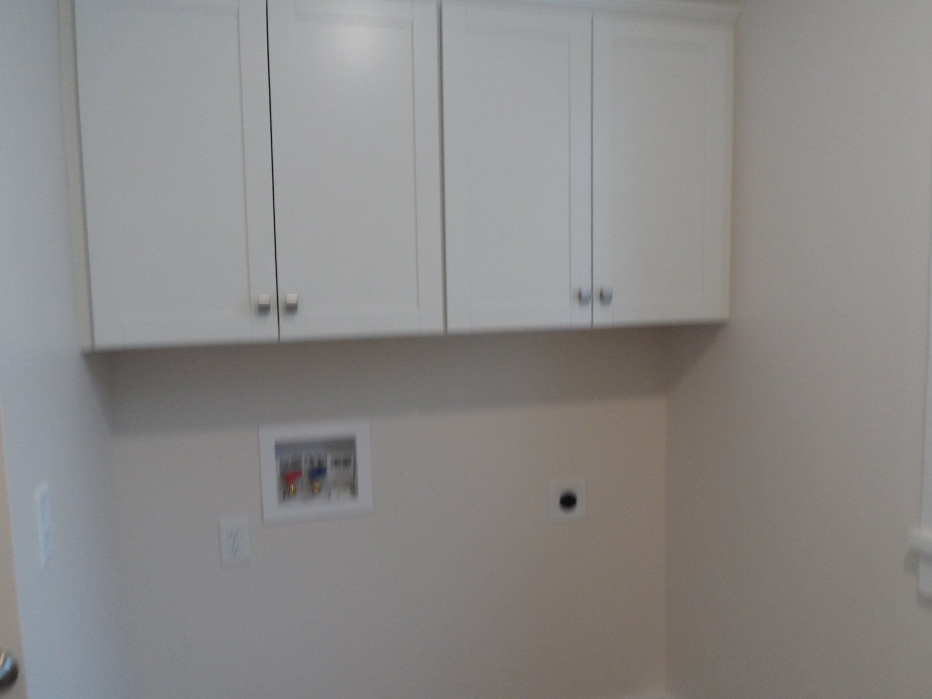A laundry room with white cabinets and a window.