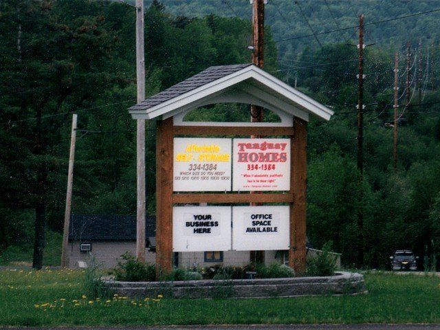 Real estate sign for Johnny Homes at roadside, with office and business listings.