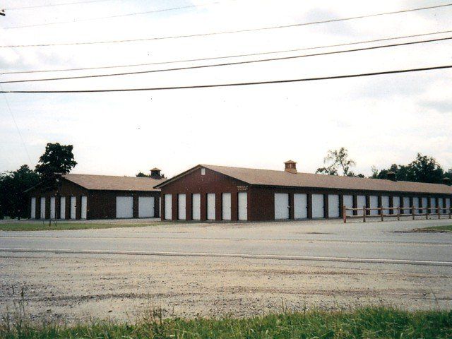 Long red-brick warehouse with white pillars under power lines beside an empty lot