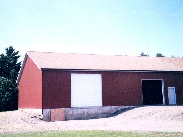Red barn-like building with white garage door, brown siding, and gravel foreground under a bright sky
