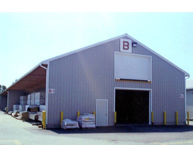 Gray warehouse building with open loading bay and stacked pallets outside