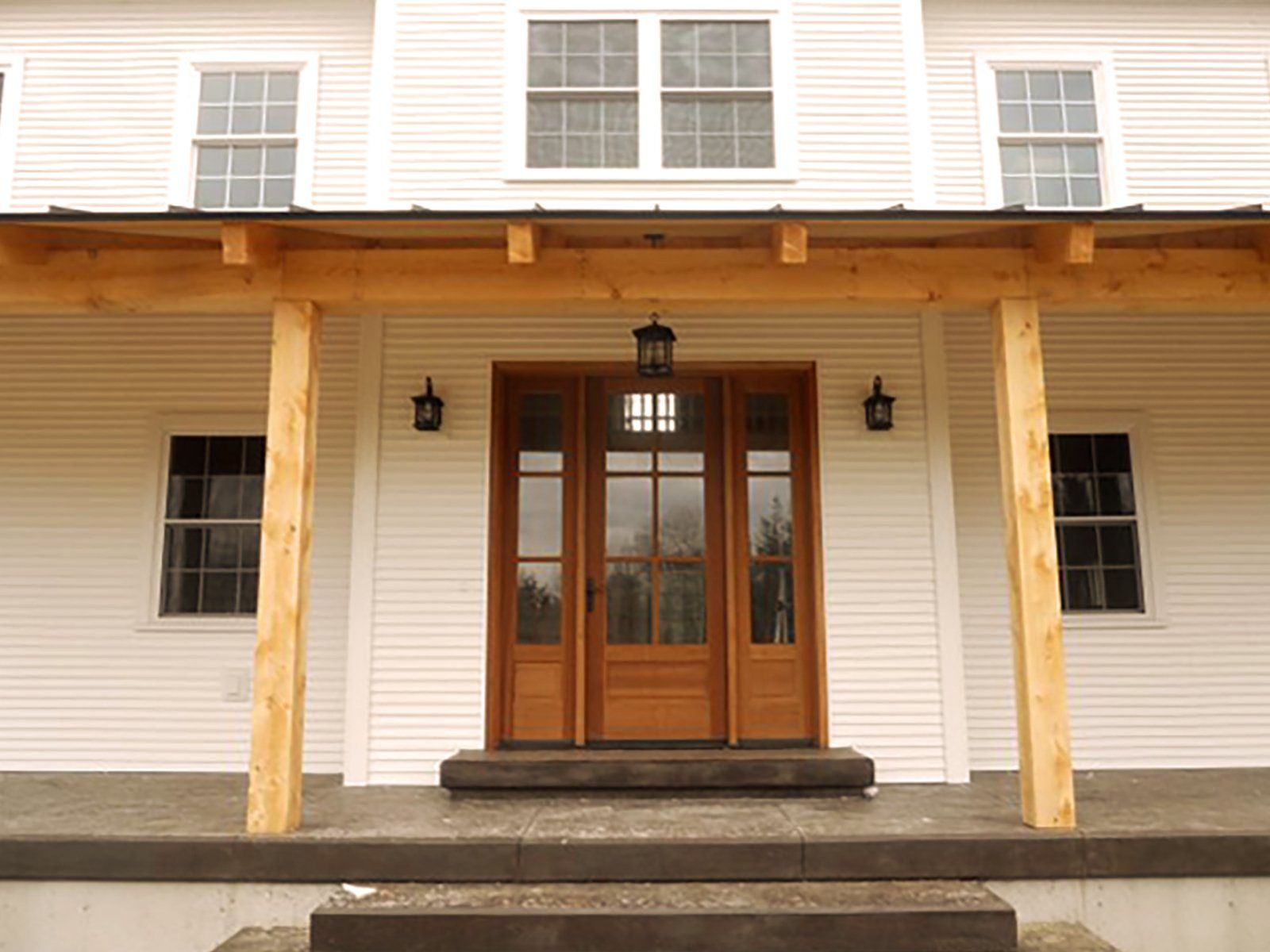 Custom efficient home building contractor in Newport, Vermont A white house with a wooden porch and a wooden door