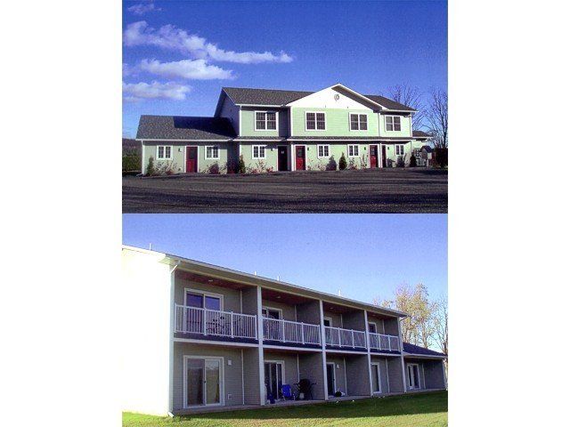 Two-story apartment buildings. One green with red doors, the other beige with balconies. Blue sky overhead.