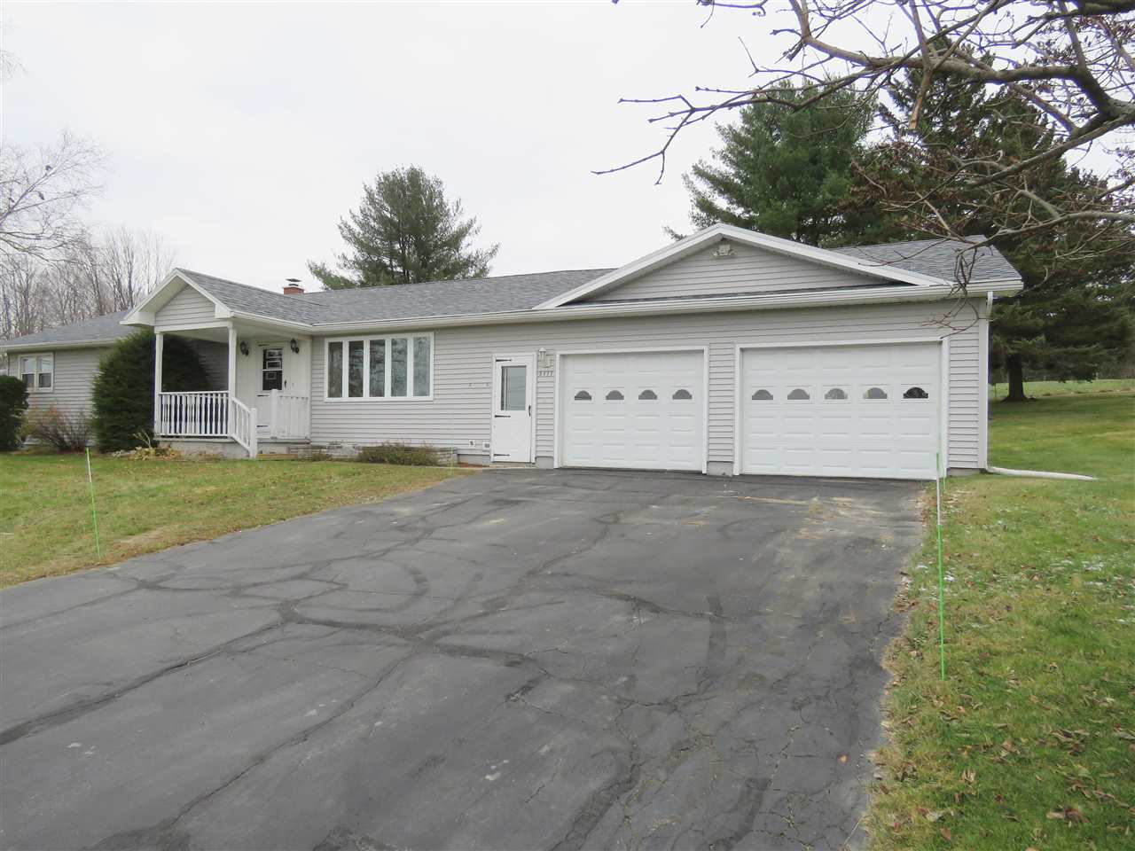 Ranch-style house with two-car garage, long asphalt driveway, cloudy sky, and grass lawn.