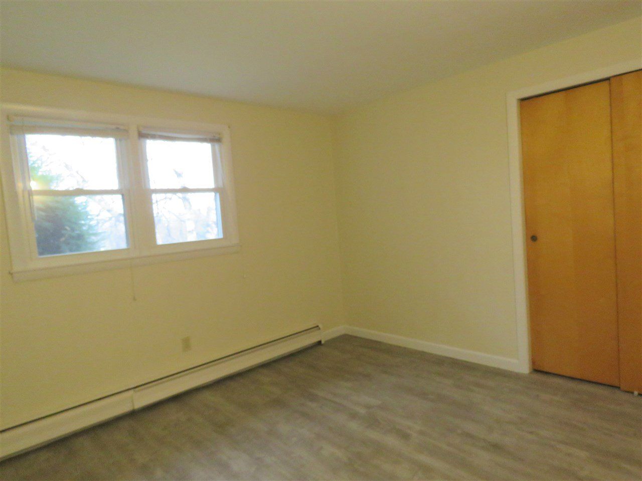 Empty room with a window, closet, and light-colored walls and flooring.