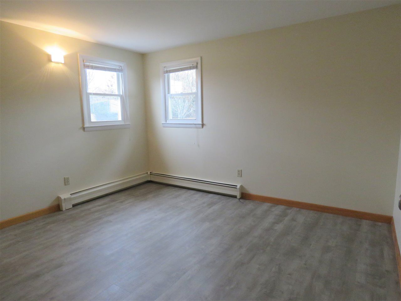 Empty room with two windows, wood-look flooring, and baseboard heater.