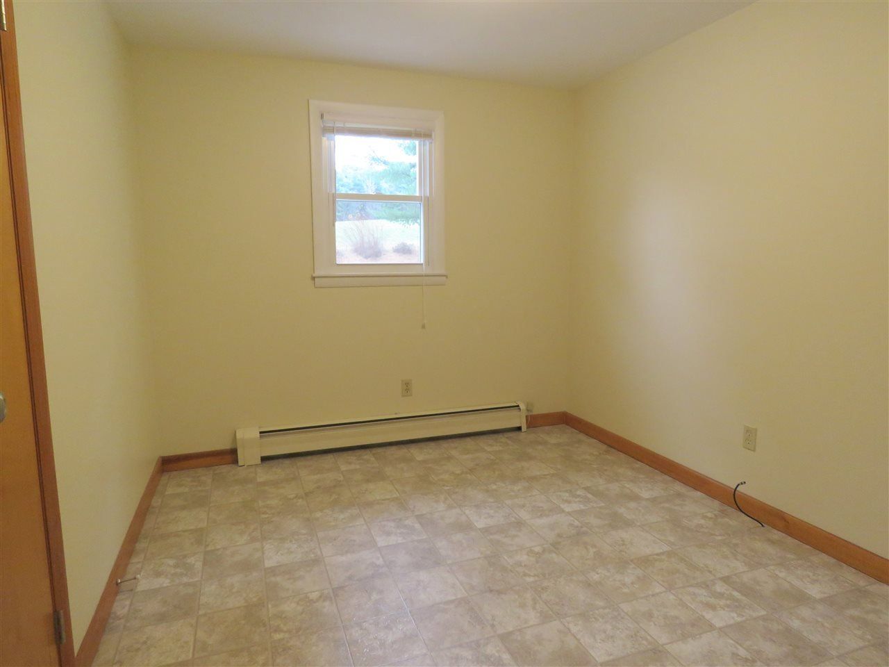 Empty room with beige walls, a small window, and tile flooring.