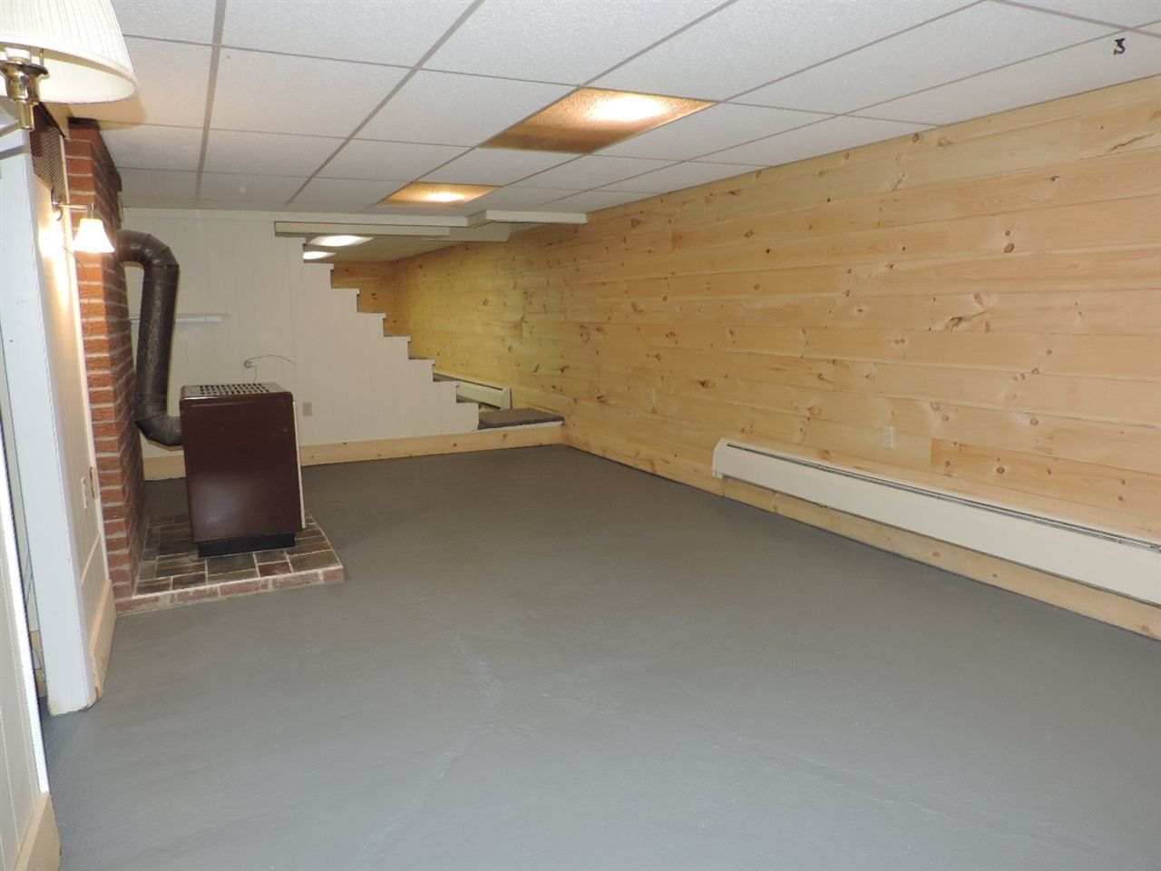 Basement with wooden wall paneling, gray floor, furnace, and exposed brick chimney.
