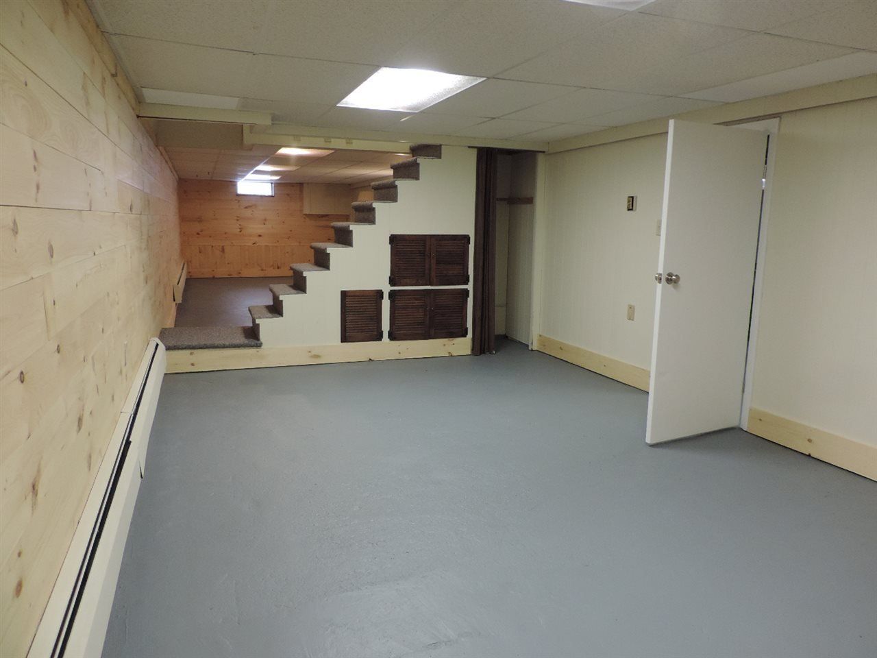 Basement with gray floor, unfinished wood walls, stairs, and a white door.