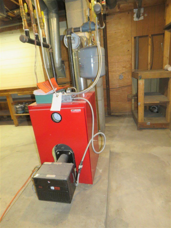 Red furnace with a gray expansion tank and metal pipes in a basement.