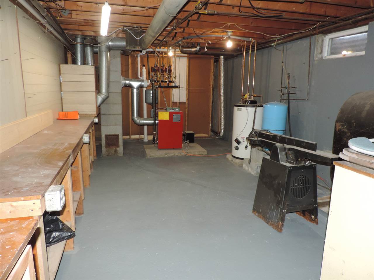 Basement with a workbench, furnace, water heater, and various equipment against gray painted walls and floor.