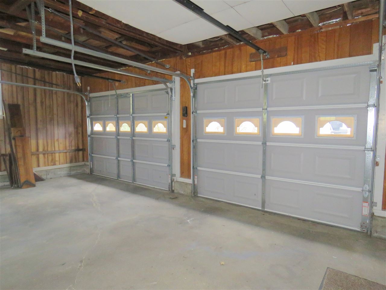 Two gray garage doors with windows in a weathered garage.