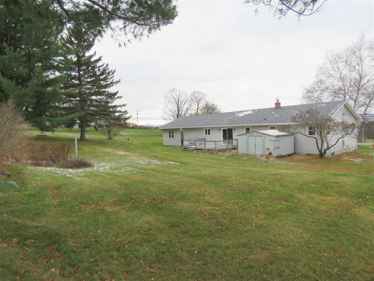 A white house with a gray roof sits on a green lawn with trees in the background. Snow flurries are visible.