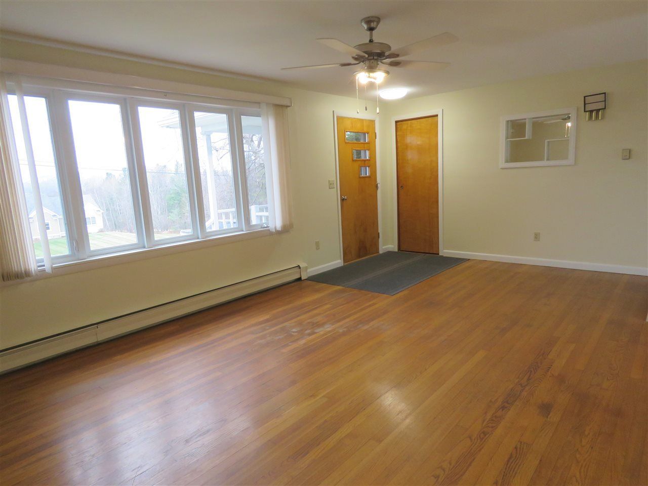 Living room with wooden floors, bay window, two doors, and a ceiling fan.