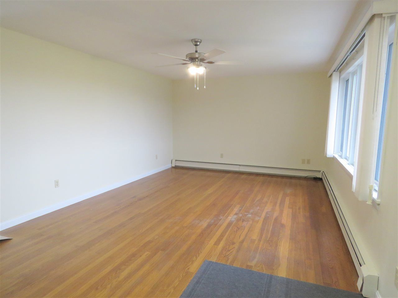 Empty room with hardwood floors, beige walls, a window, and a ceiling fan.