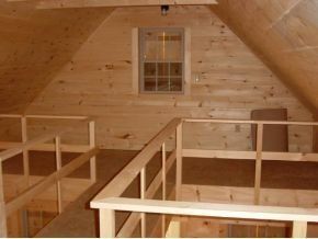 A wooden attic loft with railings, light-colored pine paneling, and a single window on the back wall.