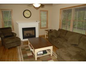 A living room with a fireplace, a brown armchair, a large sectional sofa, and a coffee table on a patterned rug.
