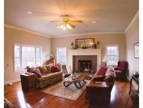 A living room with hardwood floors, a stone fireplace, a patterned sofa, a central rug, and a ceiling fan.