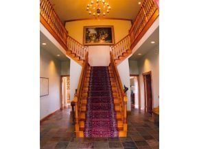 A grand staircase with a purple carpet runner ascends to a landing, flanked by wooden railings in a tiled foyer.