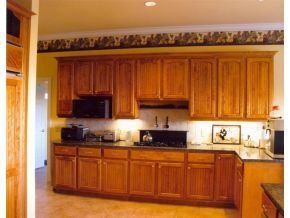Kitchen with oak cabinets, dark countertops, and a decorative wallpaper border under a ceiling with recessed lighting.