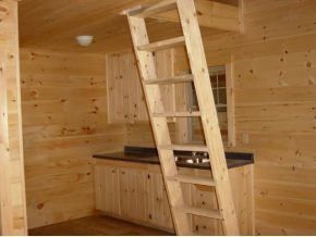 A wooden ladder leans against a kitchen counter in a rustic room with pine walls and cabinetry.