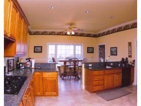 A kitchen with light wood cabinets, dark granite countertops, and a dining area with a table and chairs in the background.