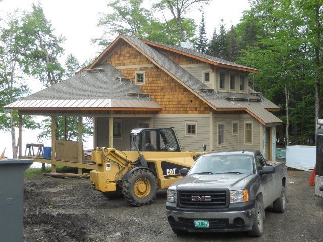 A two-story house under construction with a yellow CAT loader and a gray GMC truck parked in front.