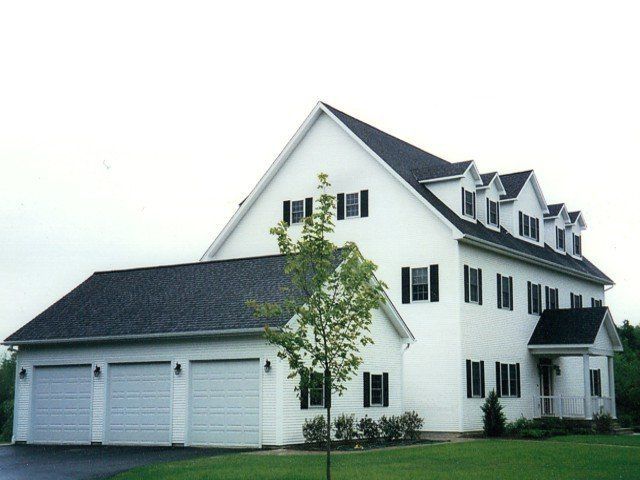 A three-story white suburban house with black shutters, a dark shingled roof, and an attached three-car garage.