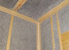 Interior wall framing with exposed wooden studs and gray cellulose insulation