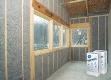 Insulated interior wall framing with windows in an unfinished room, with two construction material bags on the floor.