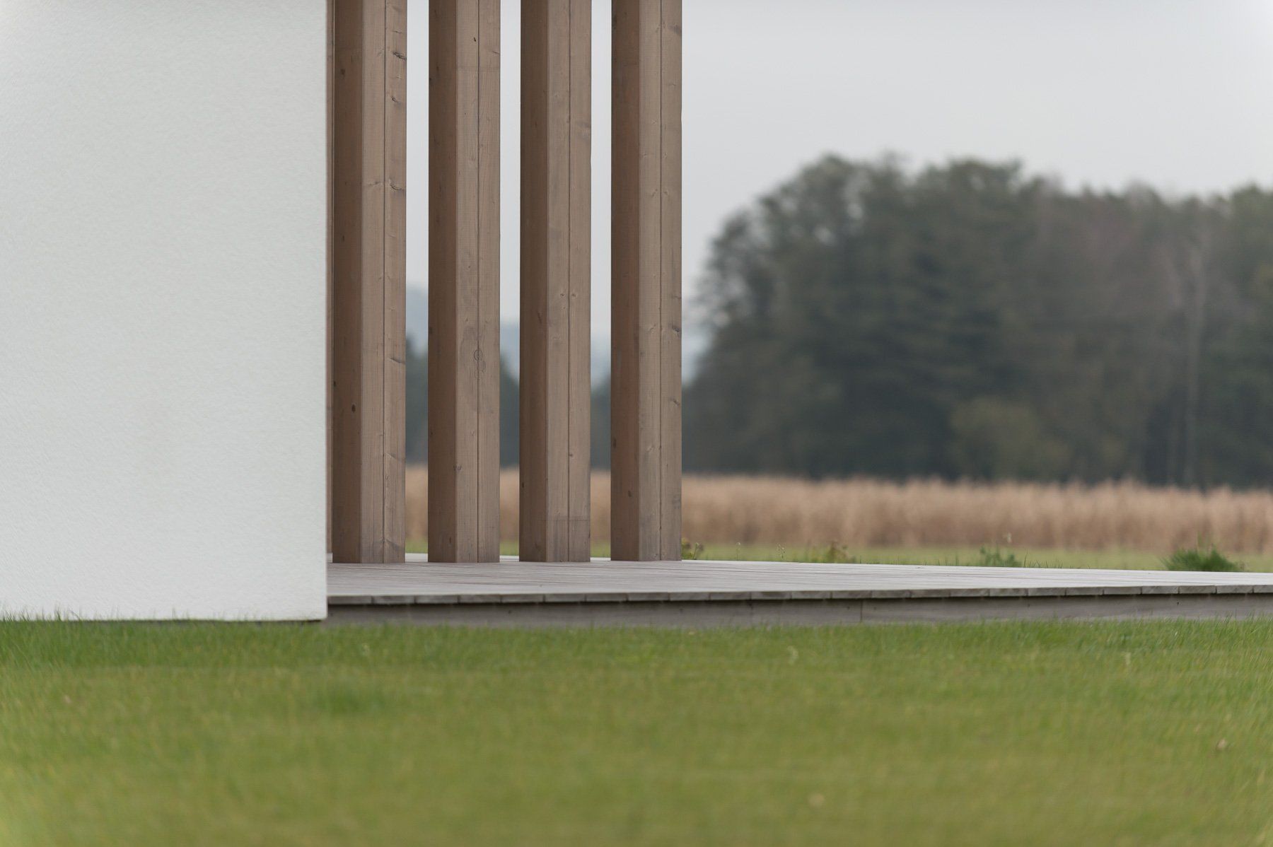 Ein weißes Gebäude mit Holzsäulen vor einem Feld.